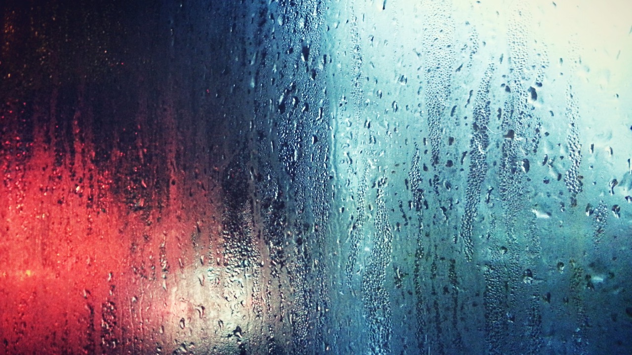 Photograph of raindrops on a window with coloured lights behind